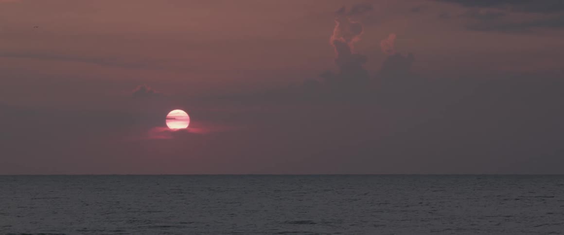 Waves rippling as the sun sets in a cloudy sky