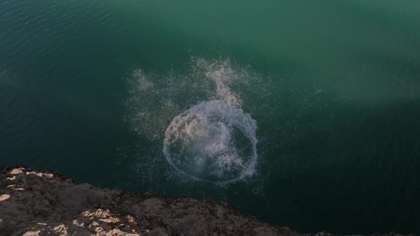 A man backflips off a cliff into a lake