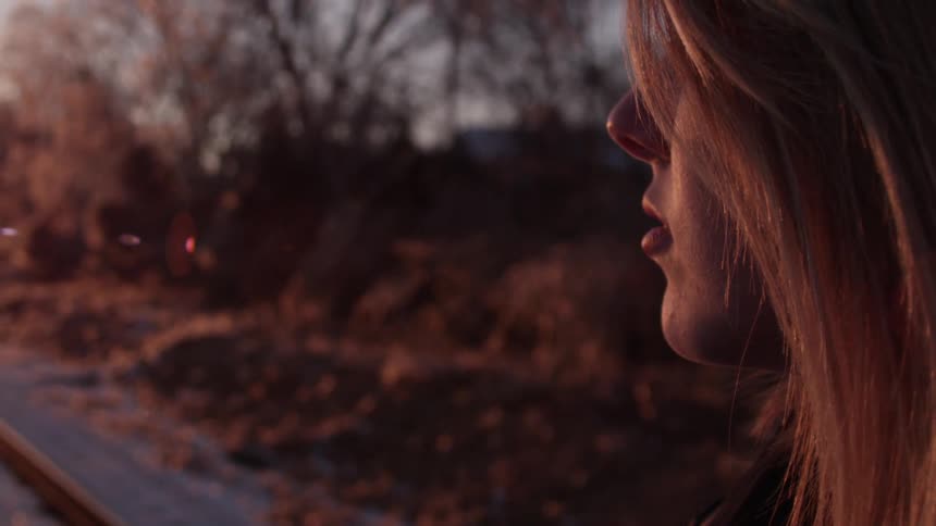 A woman standing on railroad tracks at sunset