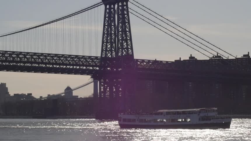 A boat floating down a river with a bridge in the background