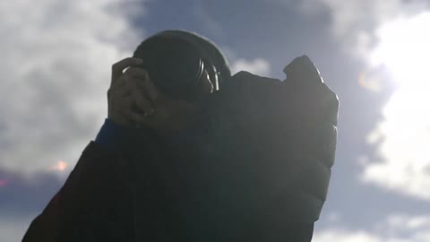 Young, blonde woman taking photographs on a cold, partially cloudy day