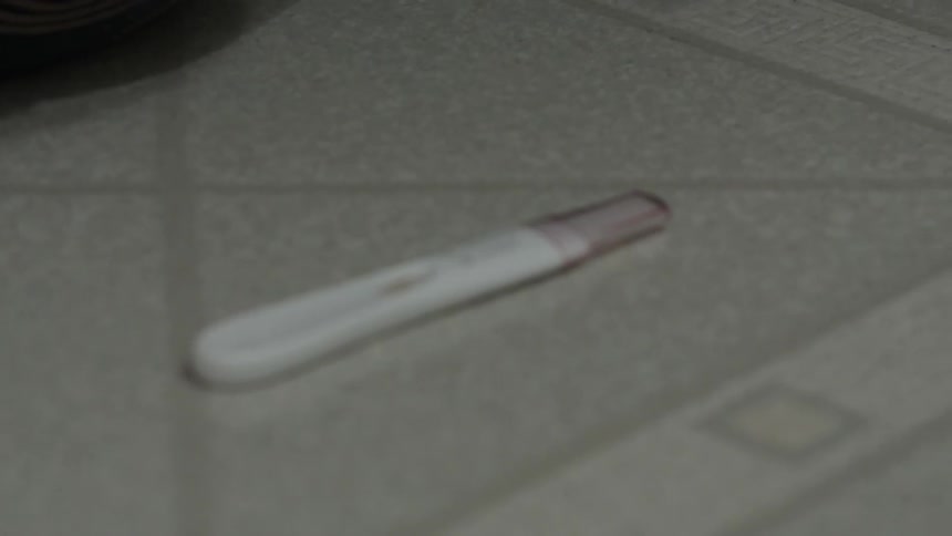 A woman cries on the bathroom floor next to a pregnancy test