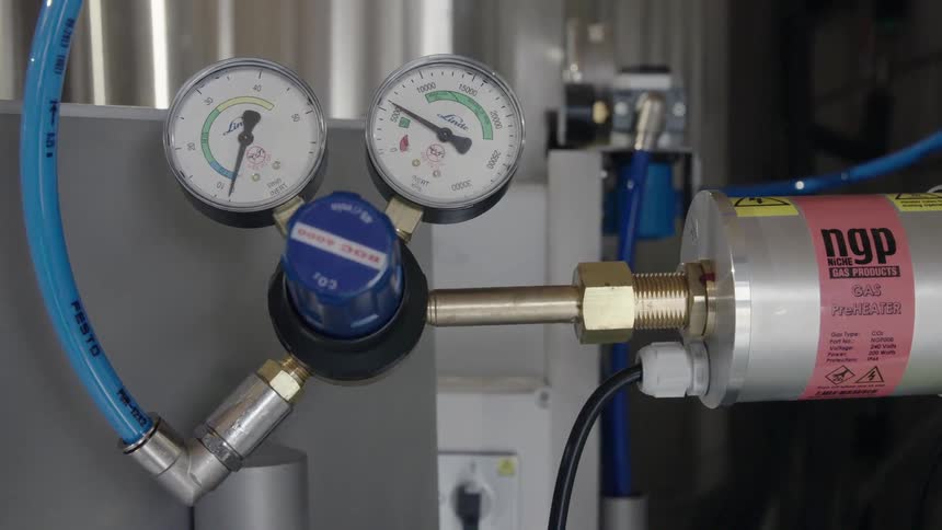 A hose is attached to industrial equipment with dial indicators