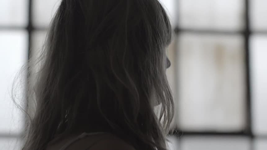 A woman stands in front of a paned window