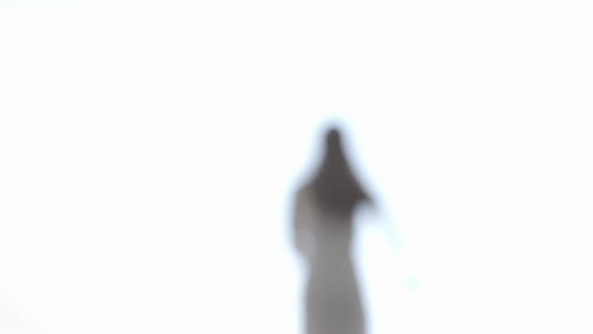 A young woman with long brown hair wearing a white dress runs into a bright light