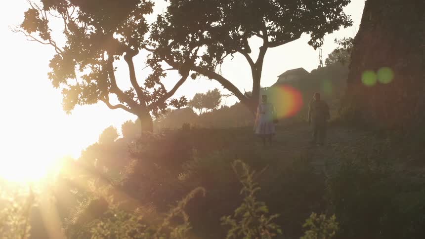 A man and woman walk down a grassy hill just before sunset