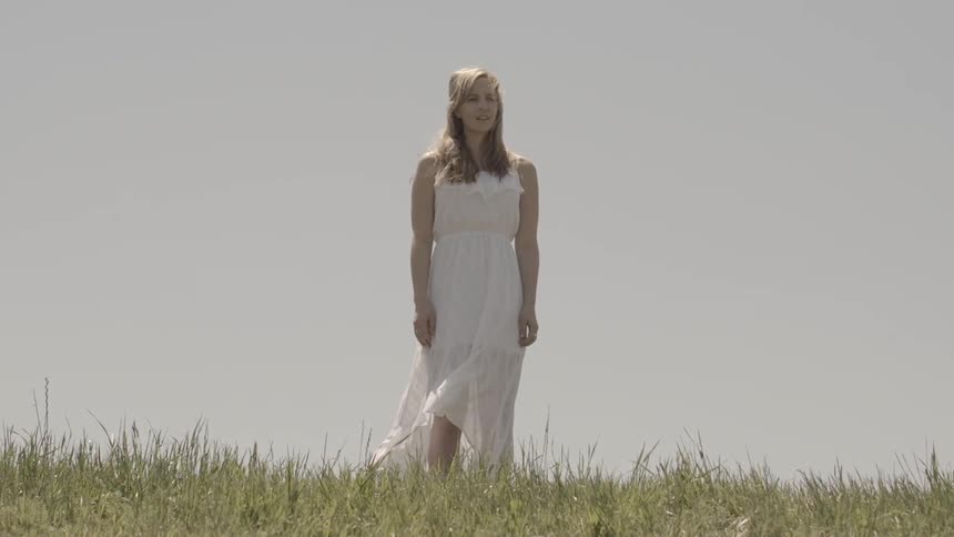 A blonde woman wearing a white dress standing in a field