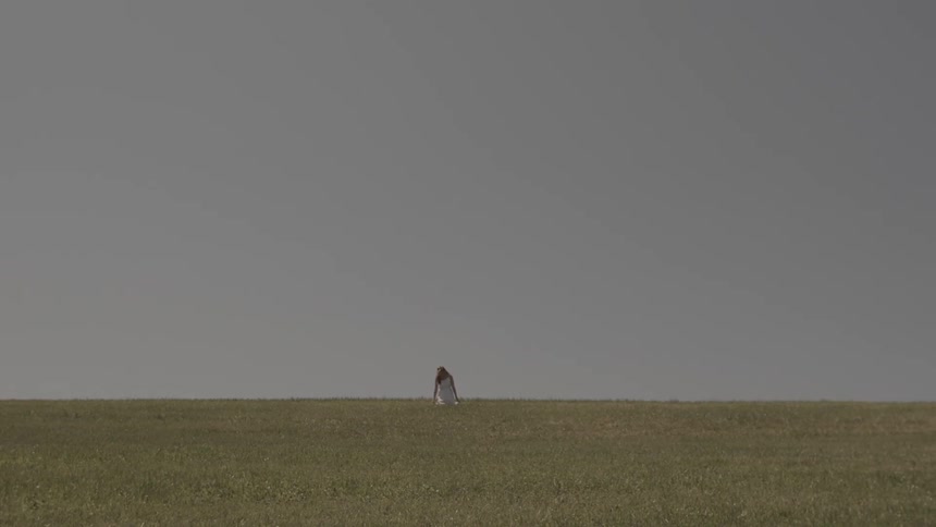A woman in a white dress running in a field and then falling to her knees