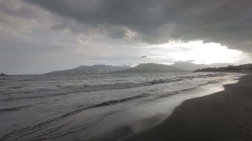 Waves crashing onto a beach under a cloudy sky
