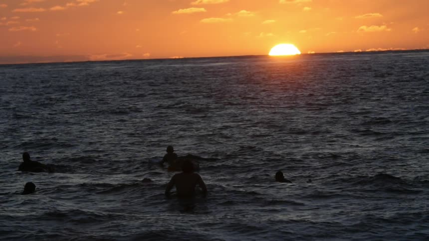Several people enjoying time in the ocean at sunset