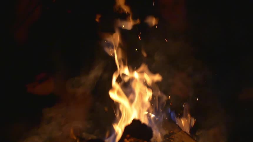 A campfire burns against the black night sky