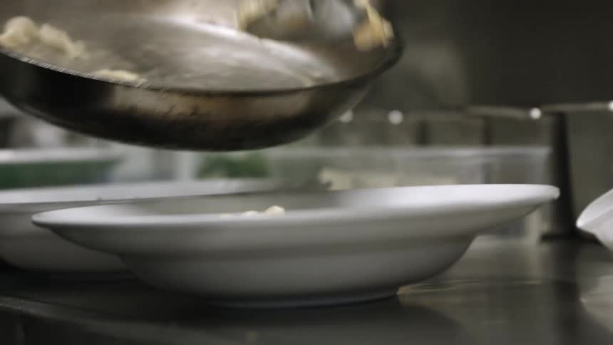 A chef scooping food from a pan into dishes