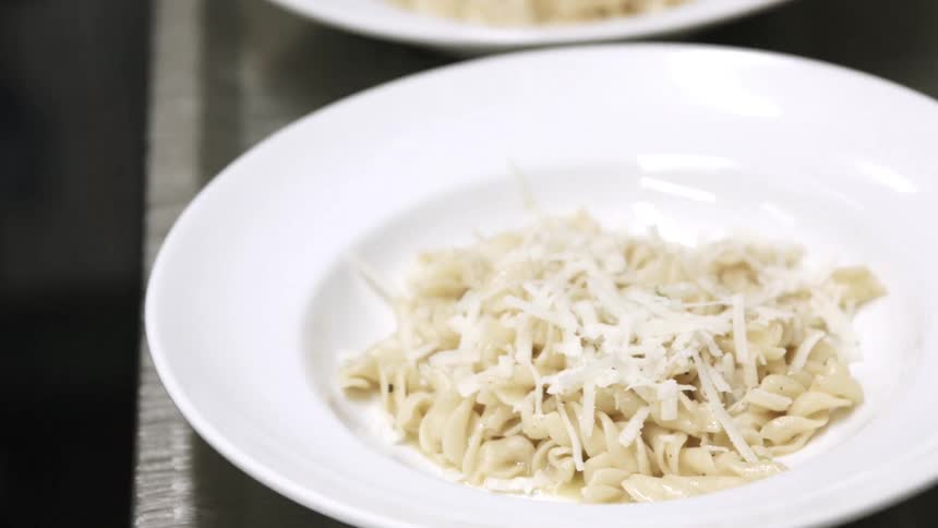 A chef sprinkling cheese on noodles in dishes