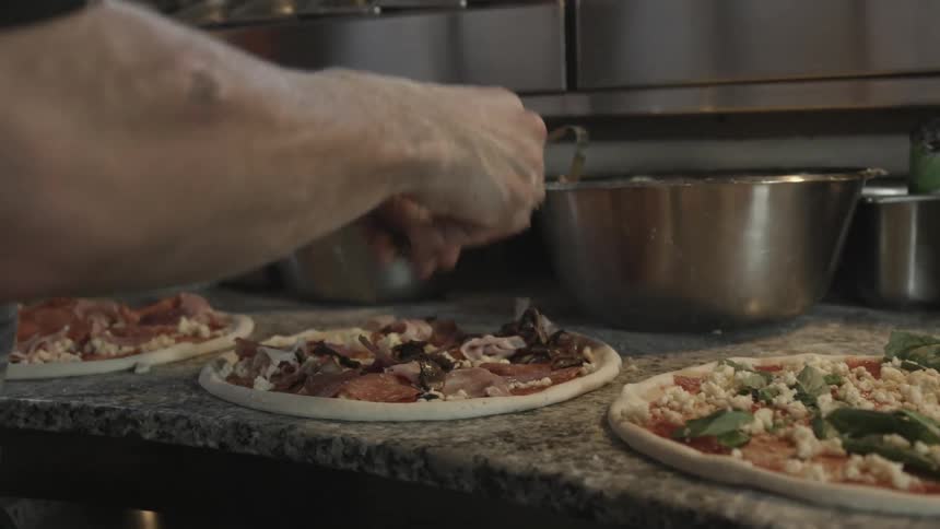 A person puts toppings on three pizzas