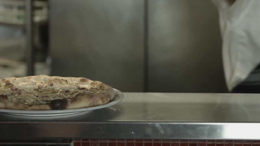 A restaurant chef places a pizza in the order window