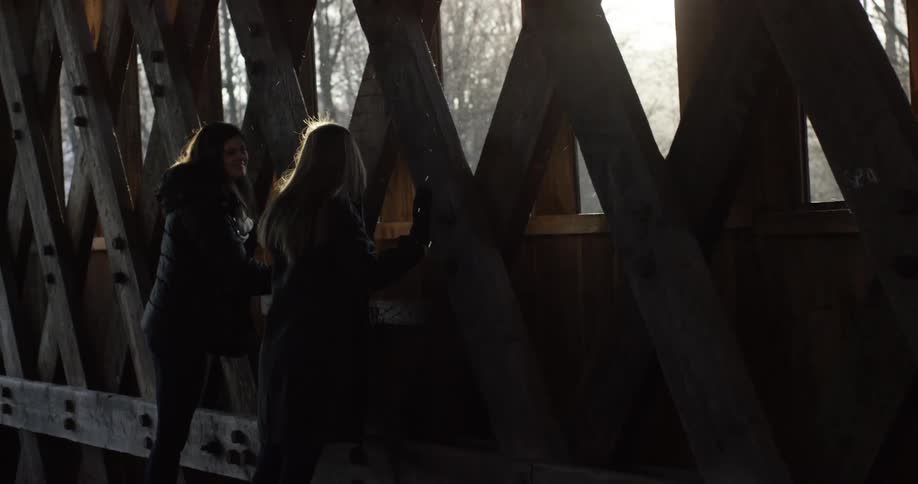 Two women look over the side of a bridge in winter