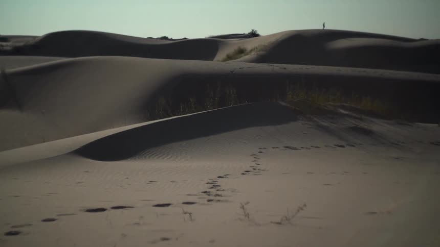 Sand dunes in desert with footprints and a person standing off in the distance