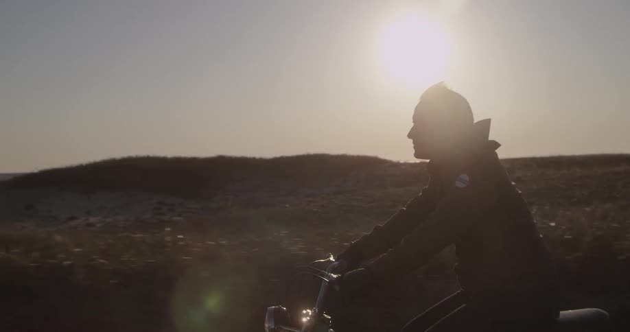 A motorcyclist rides through a sunny, rural area