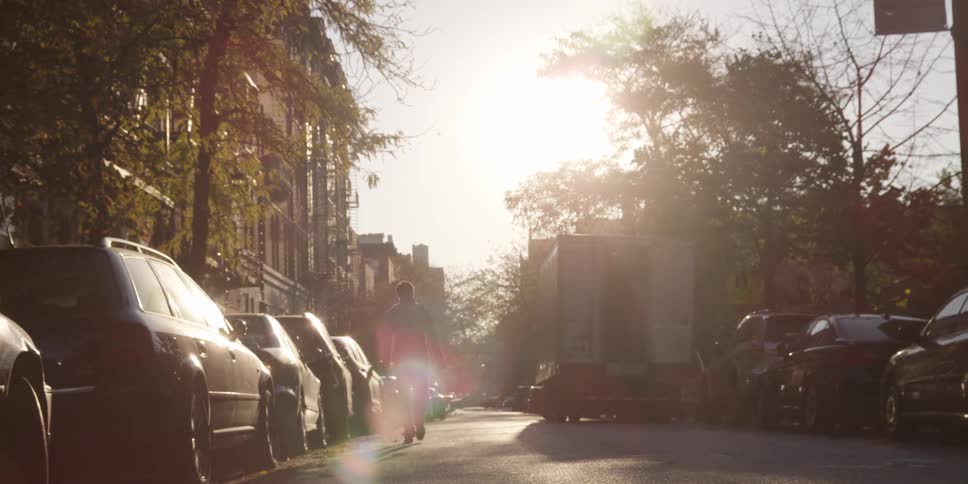 A man walks down a car-lined street