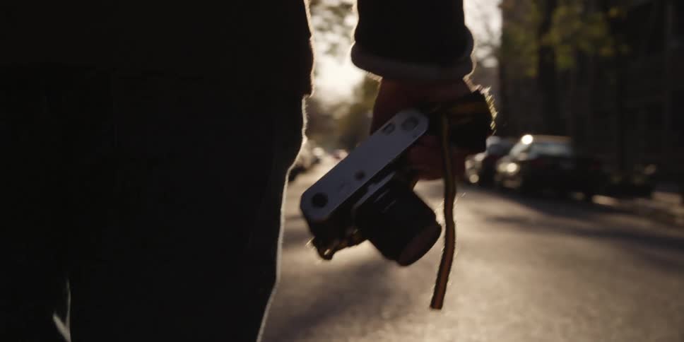 A man carries a camera down a city street