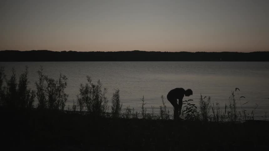 A man silhouette throwing rock into the lake