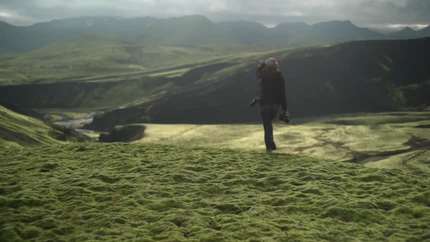 A woman with a camera walks through a sunny valley