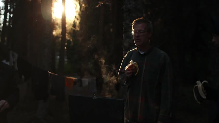 Two men stand around a campfire in a campsite