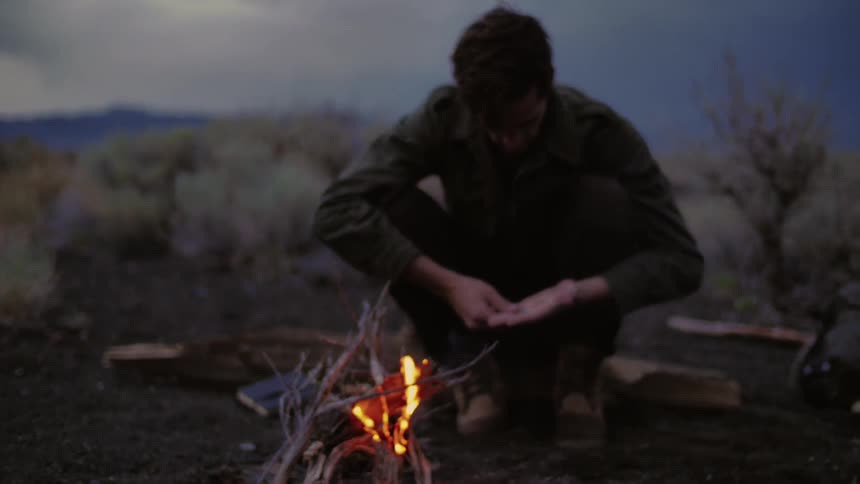 A man sits next to a campfire