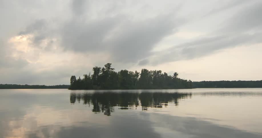 A tiny tree covered island is reflected in the waters surface