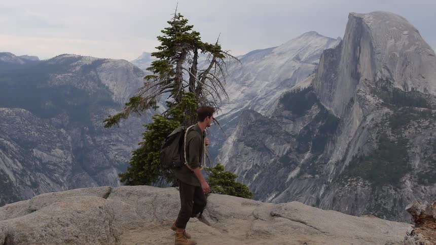 A man wearing a backpack and walking through a path in the mountains on a cloudy day