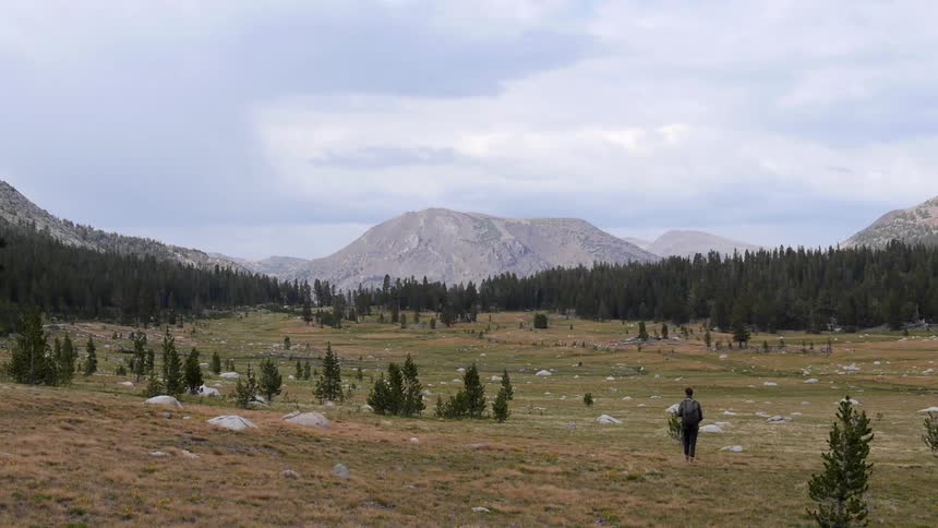 A man with a backpack walks towards a mountain
