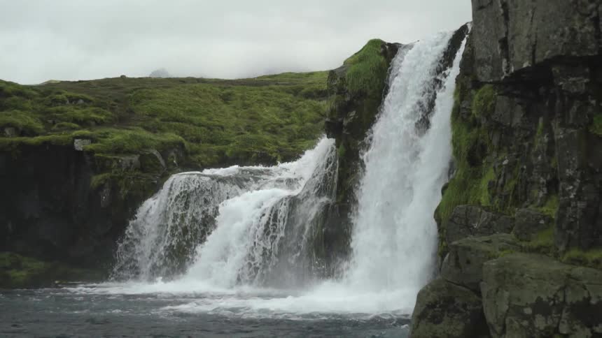 Waterfalls cascading down a grassy mountain cliff with clouds in the sky