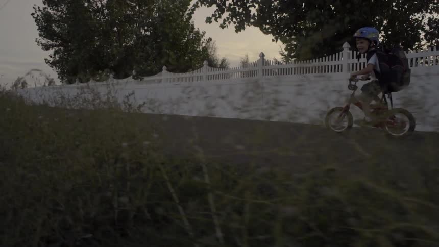 A boy with a backpack bicycles down a path