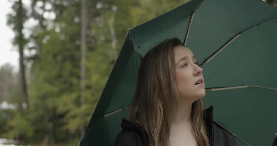 A young woman holding an umbrella and walking along a tree-lined path