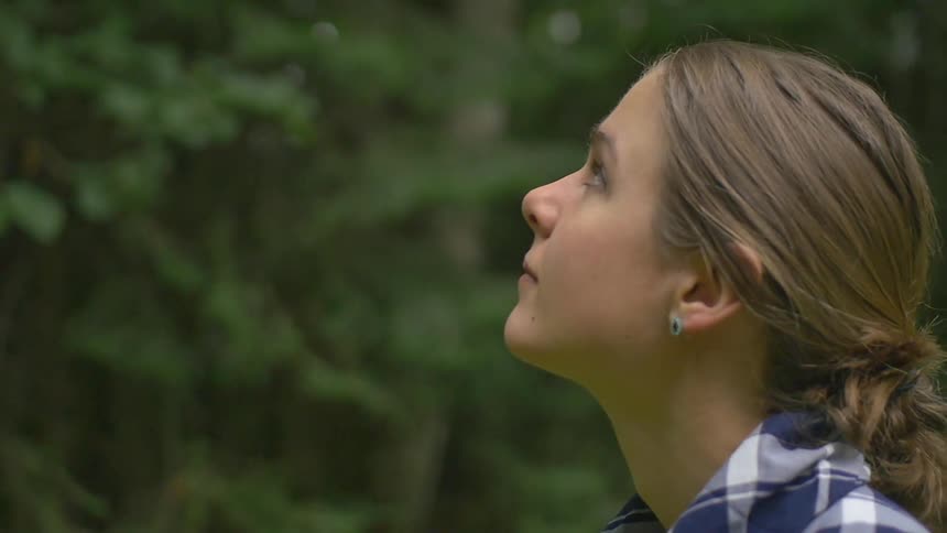 A woman walks backwards while glancing up at trees