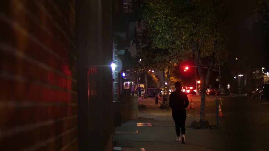 A pedestrian walks down a city street at night