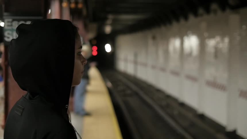 A woman in a black hoodie waits for the train
