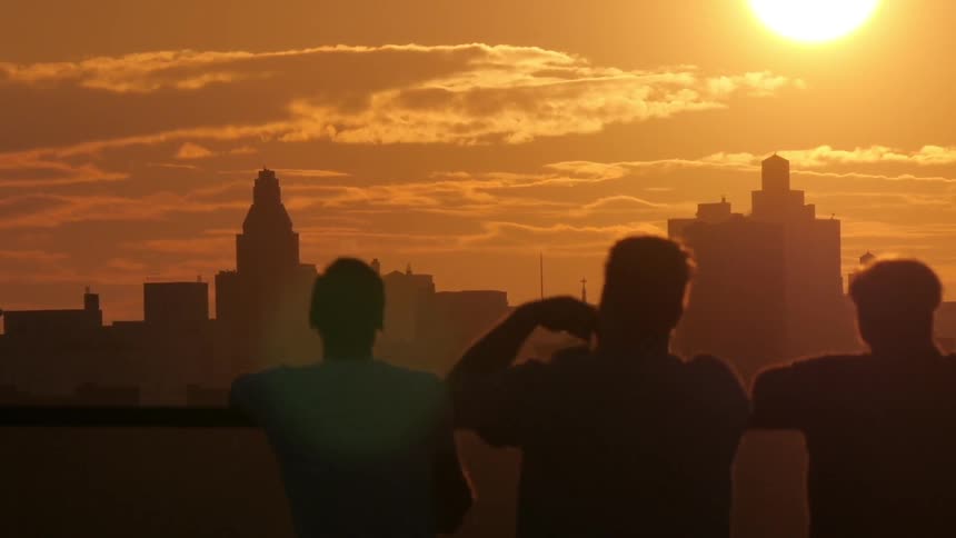 A group of friends is silhouetted against the skyline at sunset