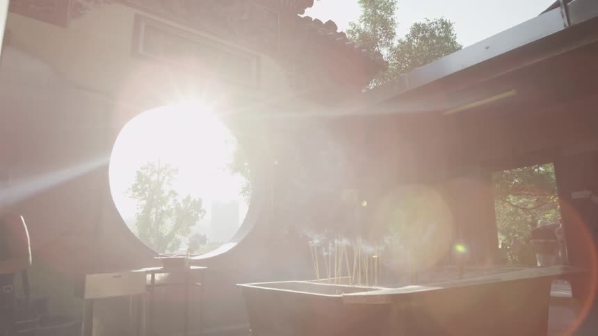 An open-air temple with incense burning and the sun beaming through a large circular window