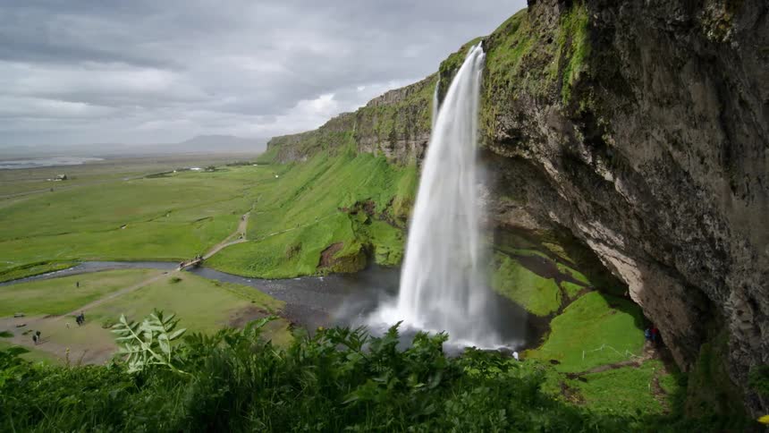A timelapse view of a waterfall cascading into a pool of water under cloudy skies