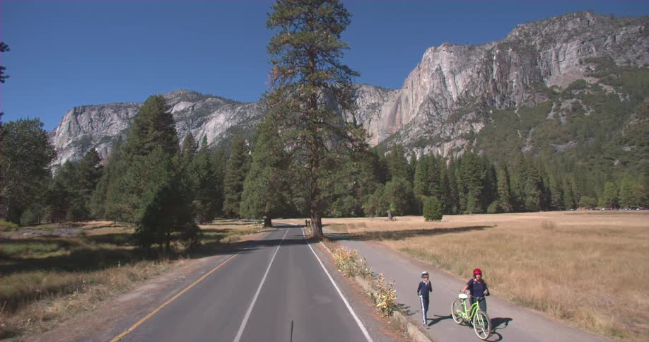 People walk down a sidewalk near a mountain