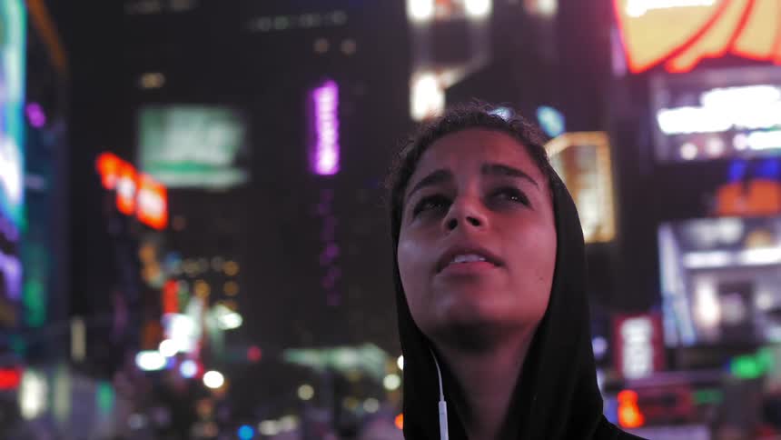 Woman in hoodie looking up at city lights