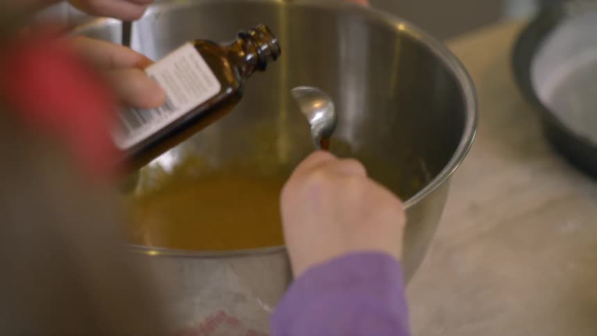 A girl pours vanilla into a mixing bowl
