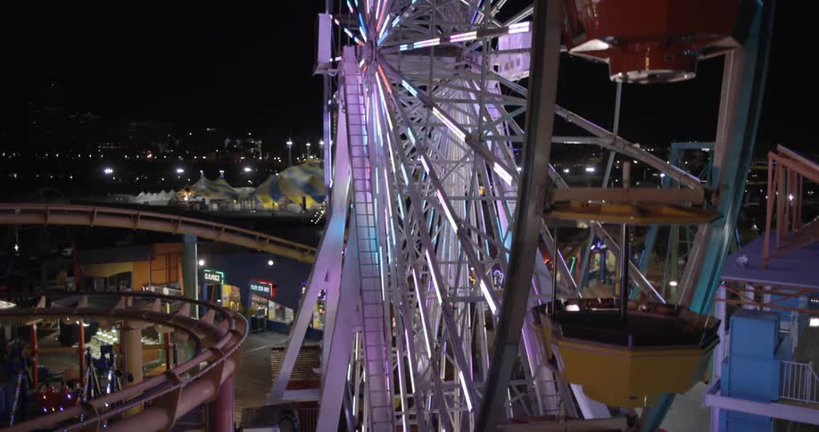 A ferris wheel lit up and turning at night over an amusement park