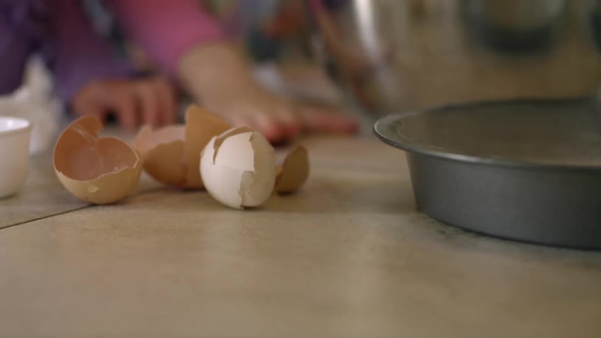Cracked eggs lie on the counter while children use other ingredients in the background