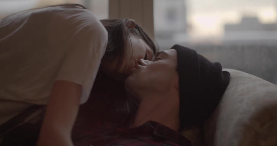 A young man and woman fall onto a couch to kiss