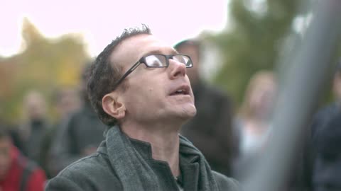 A man standing outside looking up with a crowd of people behind him