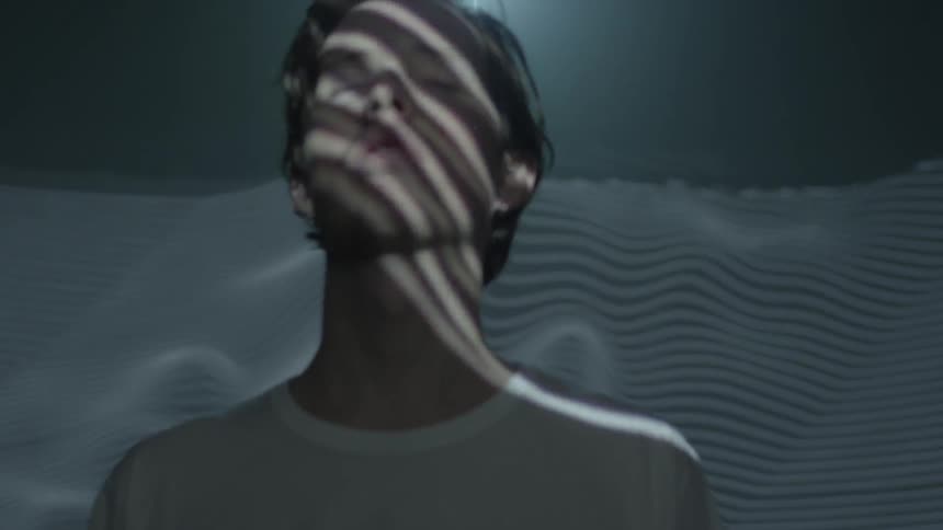 A man standing with his eyes closed has waves reflecting on his face