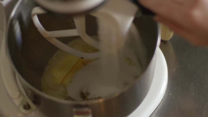 Sugar is being poured into a mixing bowl that already holds other cake ingredients