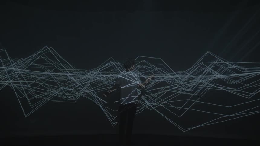A man stand amidst a projection of lights flashing in wave patterns